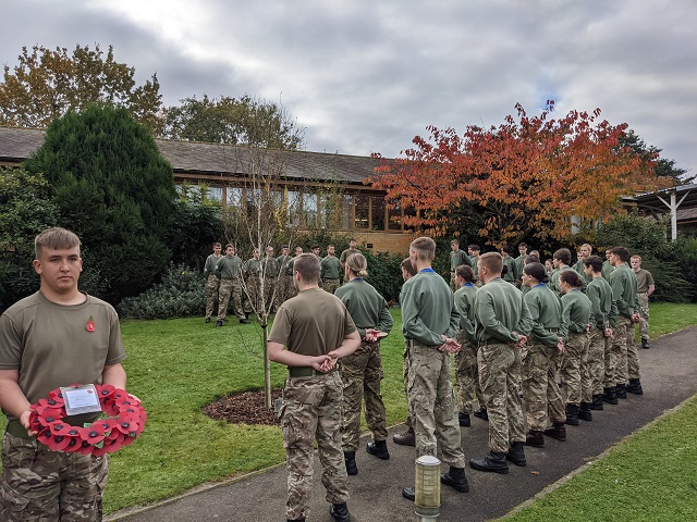 Students in armed forces uniform gather around the memorial tree
