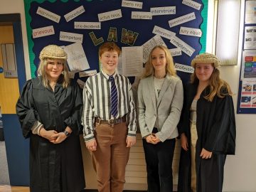 Four students in front of a Law sign, with two dressed in gowns and wigs