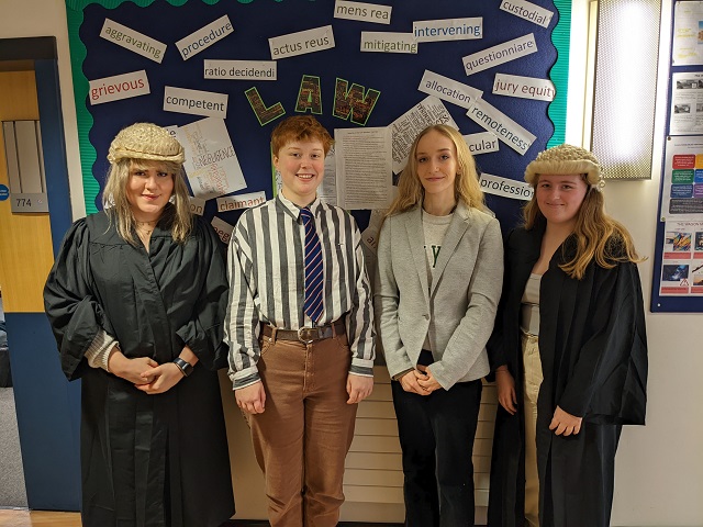 Four students in front of a Law sign, with two dressed in gowns and wigs